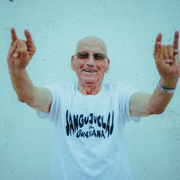 Hombre mayor con gafas y camiseta de Sanguijuelas del Guadiana levanta ambos brazos haciendo el gesto de los cuernos