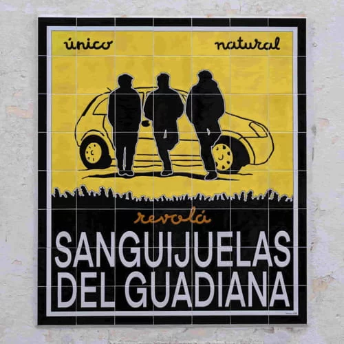 Mural de azulejos amarillos y negros de Sanguijuelas del Guadiana, con tres siluetas frente a un coche y los textos “único”, “natural” y “revolá